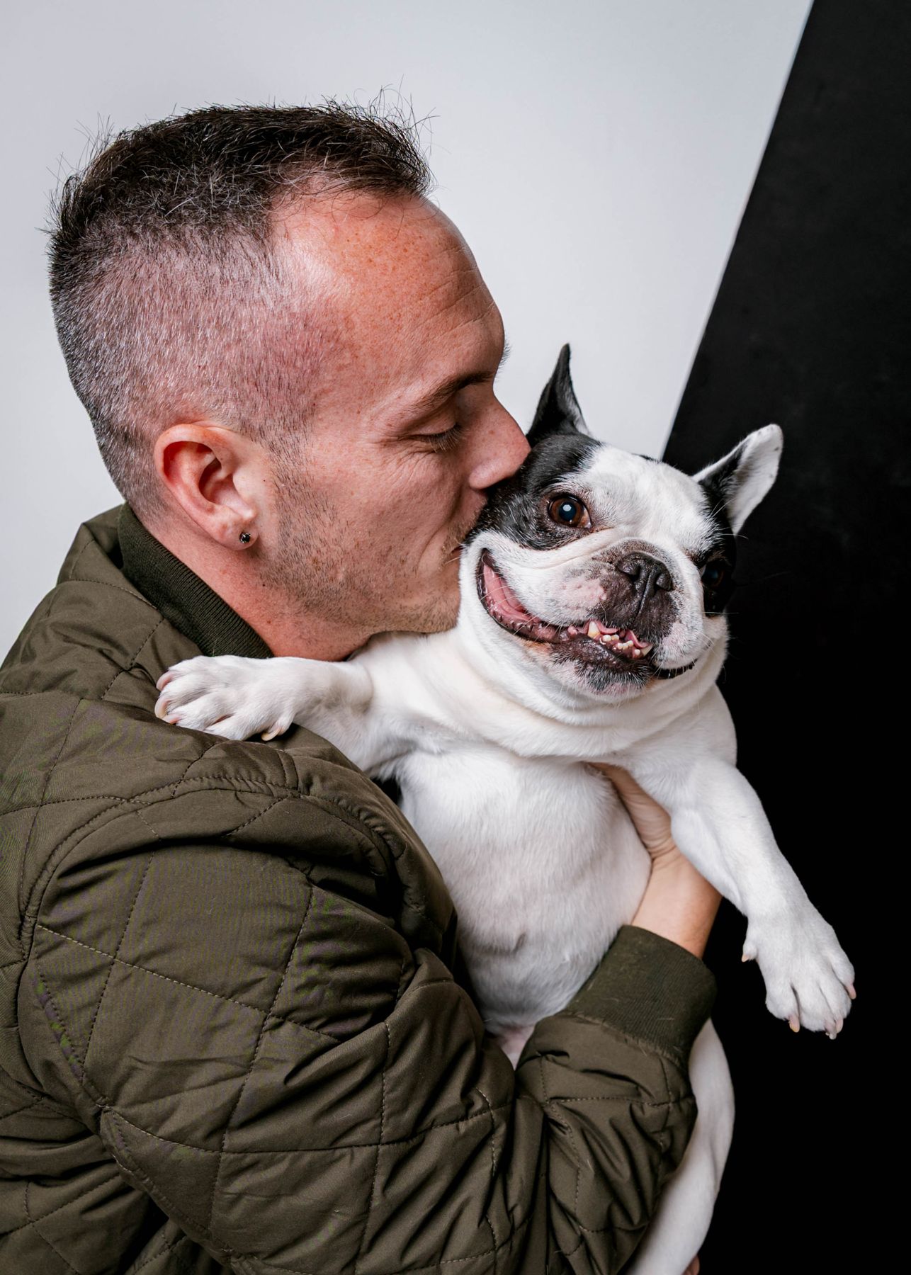 Tyler laughing as Leo, a black and white French Bulldog, licks his cheek