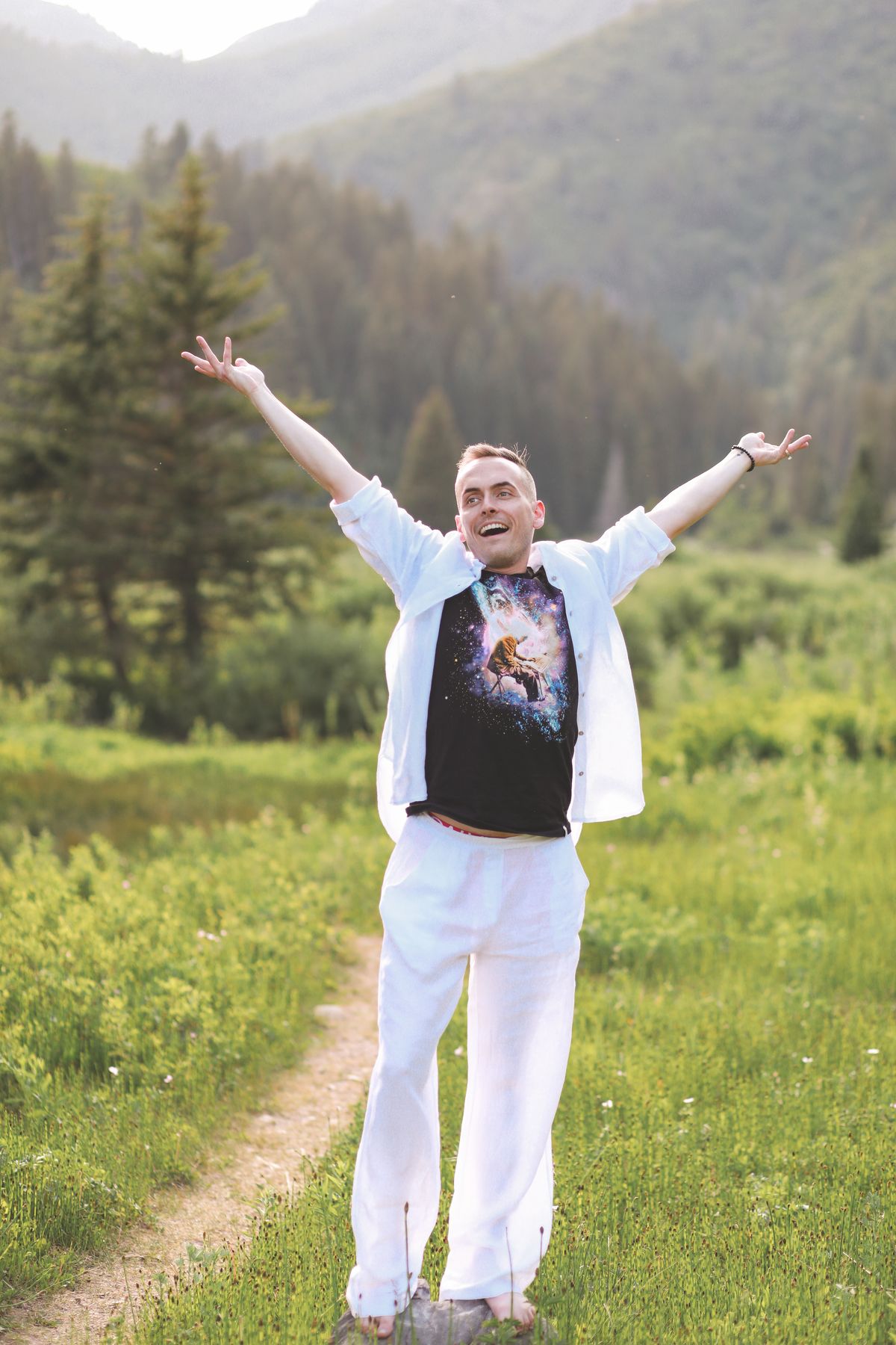 Tyler standing in a mountain meadow with his arms open wide