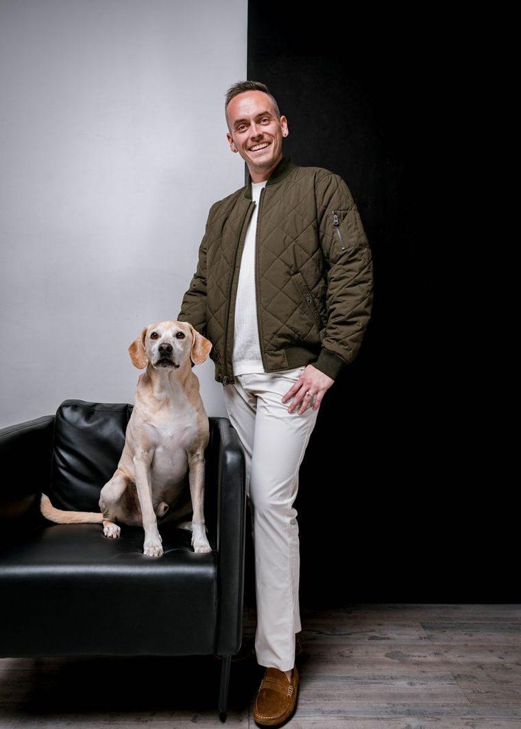 Tyler standing beside Banksy, his bigger dog, who sits on a black leather chair