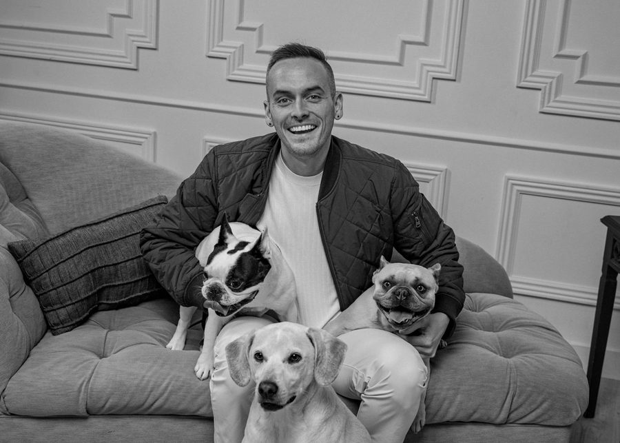 Black and white photo of Tyler smiling on a sofa with Leo, Daisy and Banksy